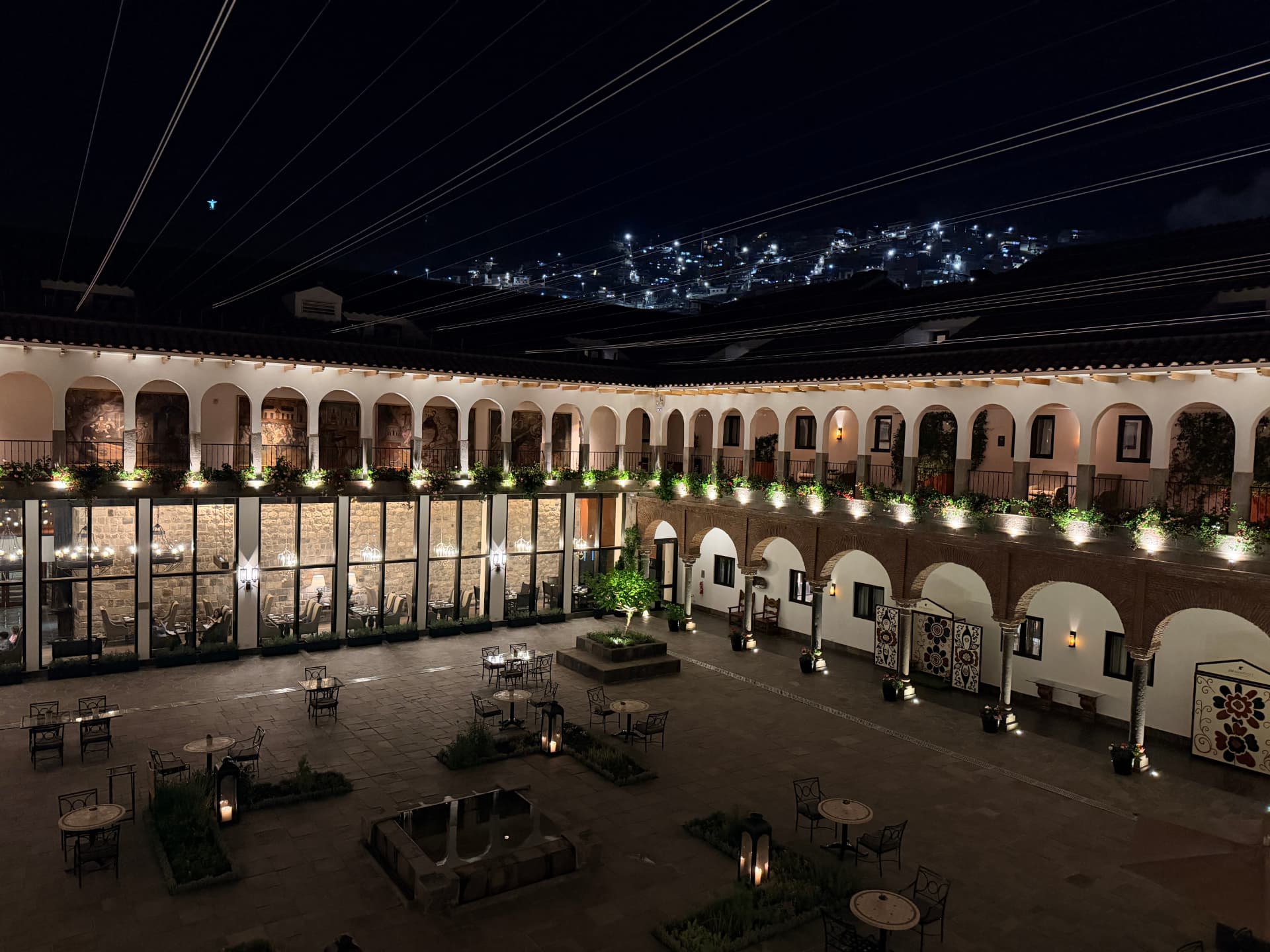 Arched colonial courtyard in Cusco at night with hillside lights beyond