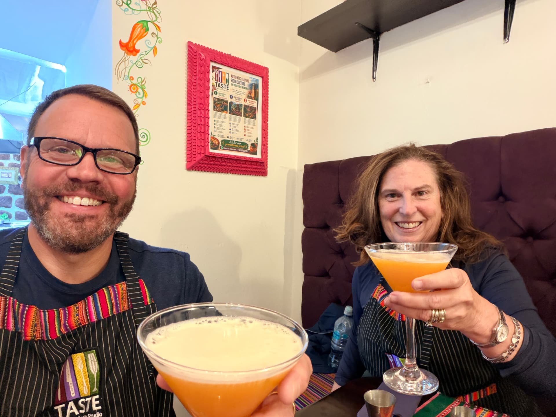 Kevin and Joan in striped aprons toasting pisco sours at a cooking class