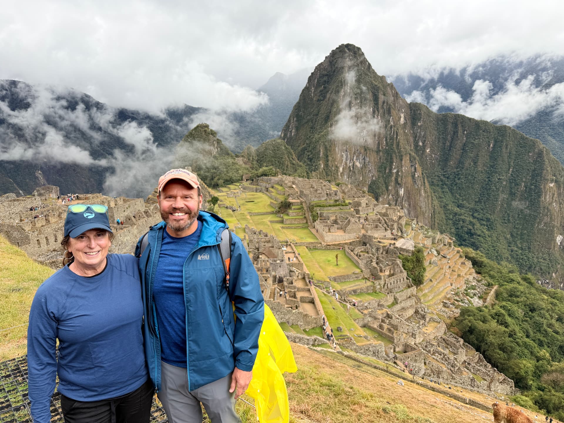 Kevin and Joan smiling in front of the Machu Picchu citadel with Huayna Picchu in the clouds behind