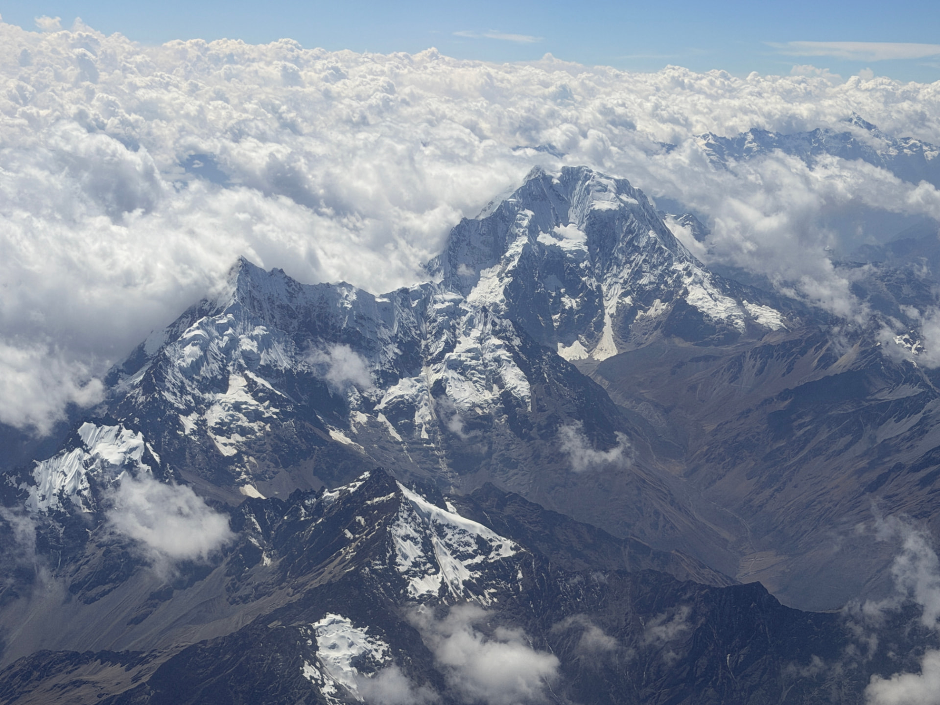 Snow-covered Andean peaks rising above a sea of clouds seen from the plane