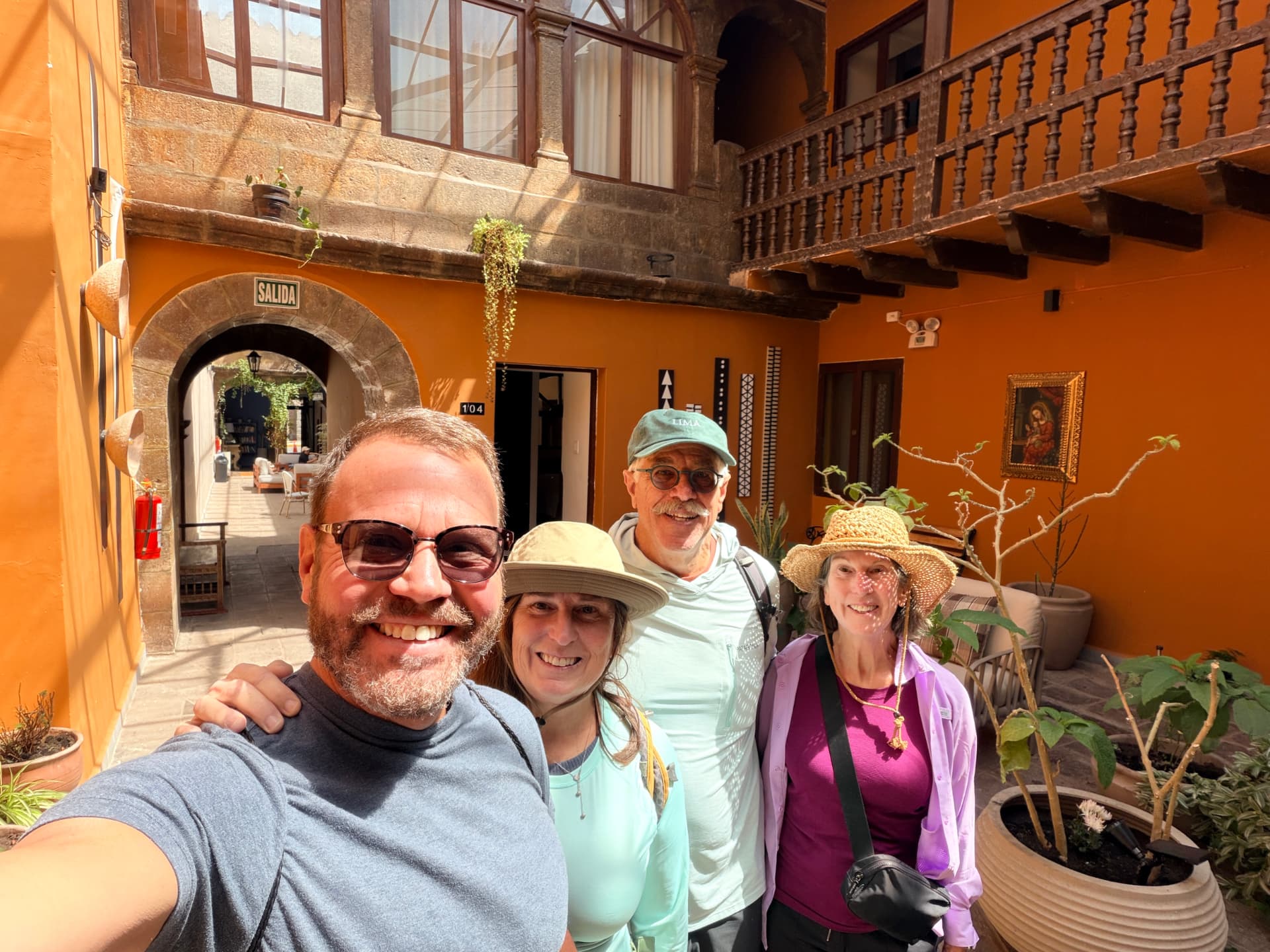 Kevin, Joan, Ed and Kathy smiling in a sunlit ochre colonial courtyard in Cusco