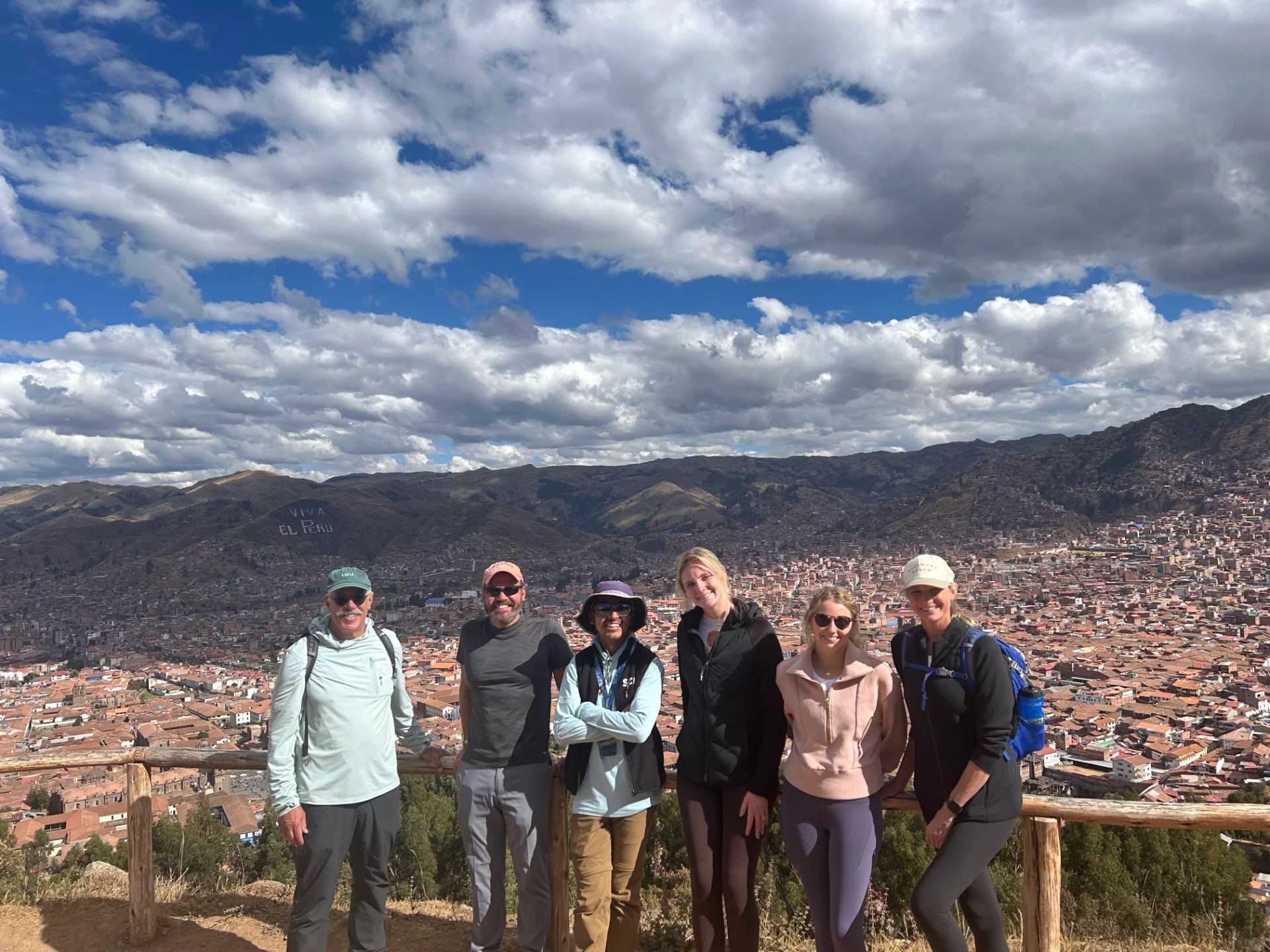 The group at a wooden railing overlooking the red rooftops of Cusco with VIVA EL PERU on the hillside